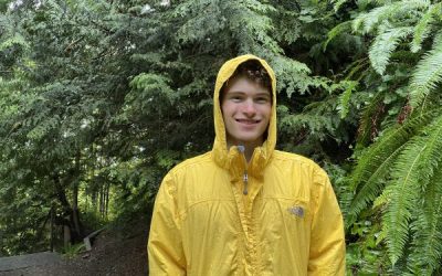 Image shows Ben Agro wearing a yellow raincoat infront of trees.