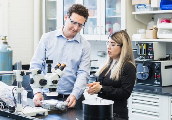 A professor and a student using a microscope.